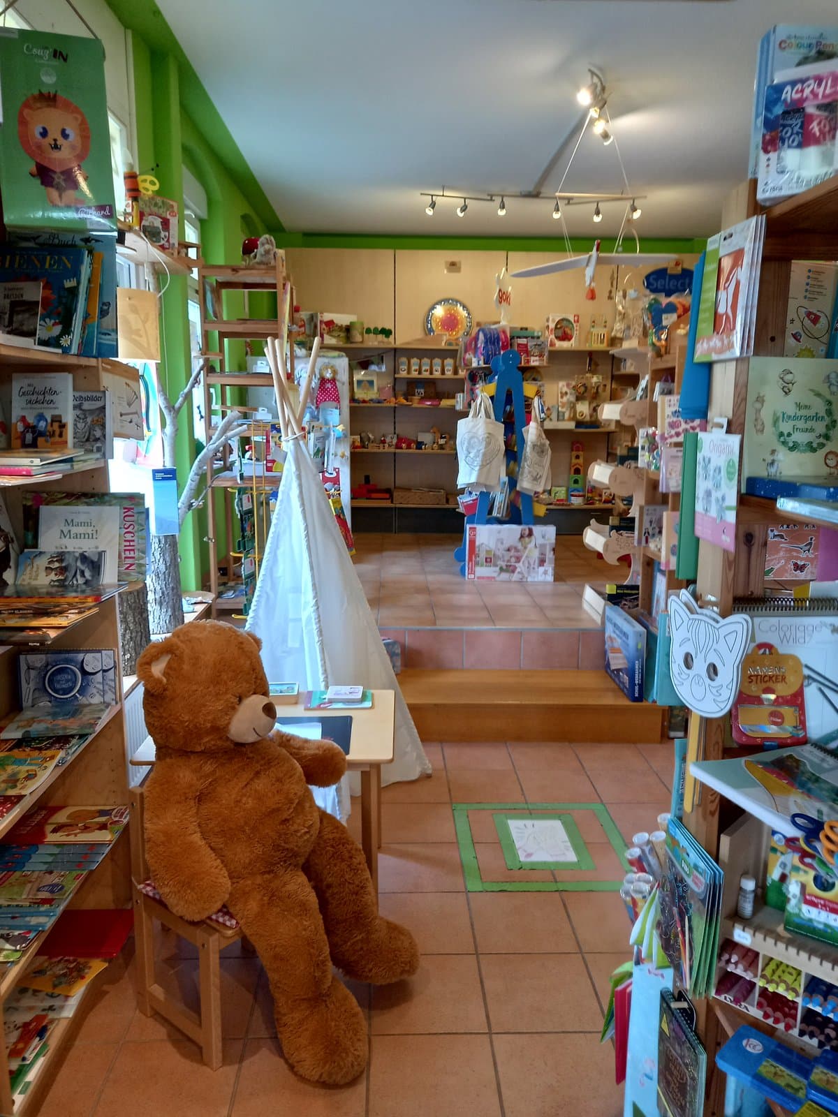 Ladenraum mit Tipi, großem Plüschbär am Kindertisch und Bilderbuch-Regalen